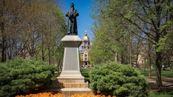 a statue of Notre Dame founder Rev. Edward Sorin, C.S.C., with the Golden Dome in the background on a sunny spring day