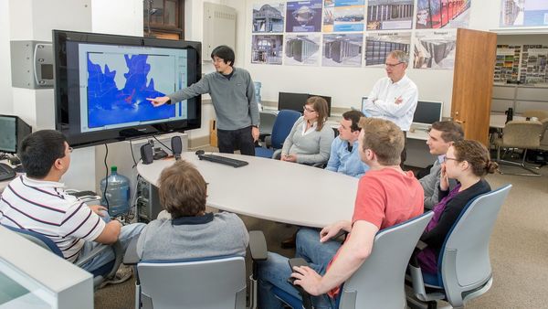 inside the Westerink civil engineering lab, with a student pointing to items on a screen as Professor Joannes Westerink (standing) and others look on