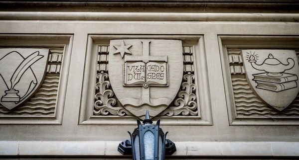 relief above door to O'Shaughnessy Hall, featuring the University seal in the middle with a quill and paper to the left and a lamp atop books on the right